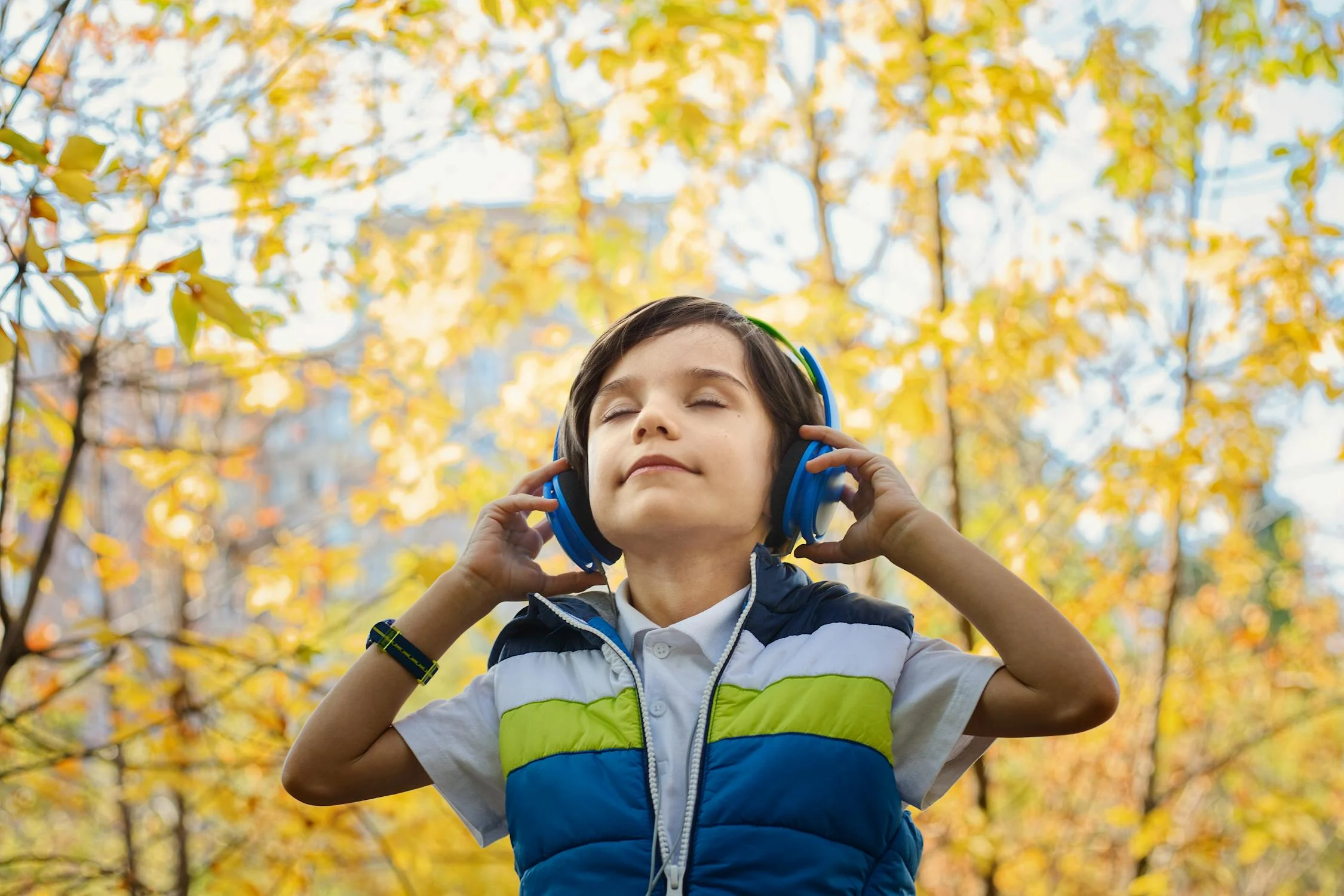 Kind mit geschlossenen Augen hört draußen Musik über blaue Kopfhörer