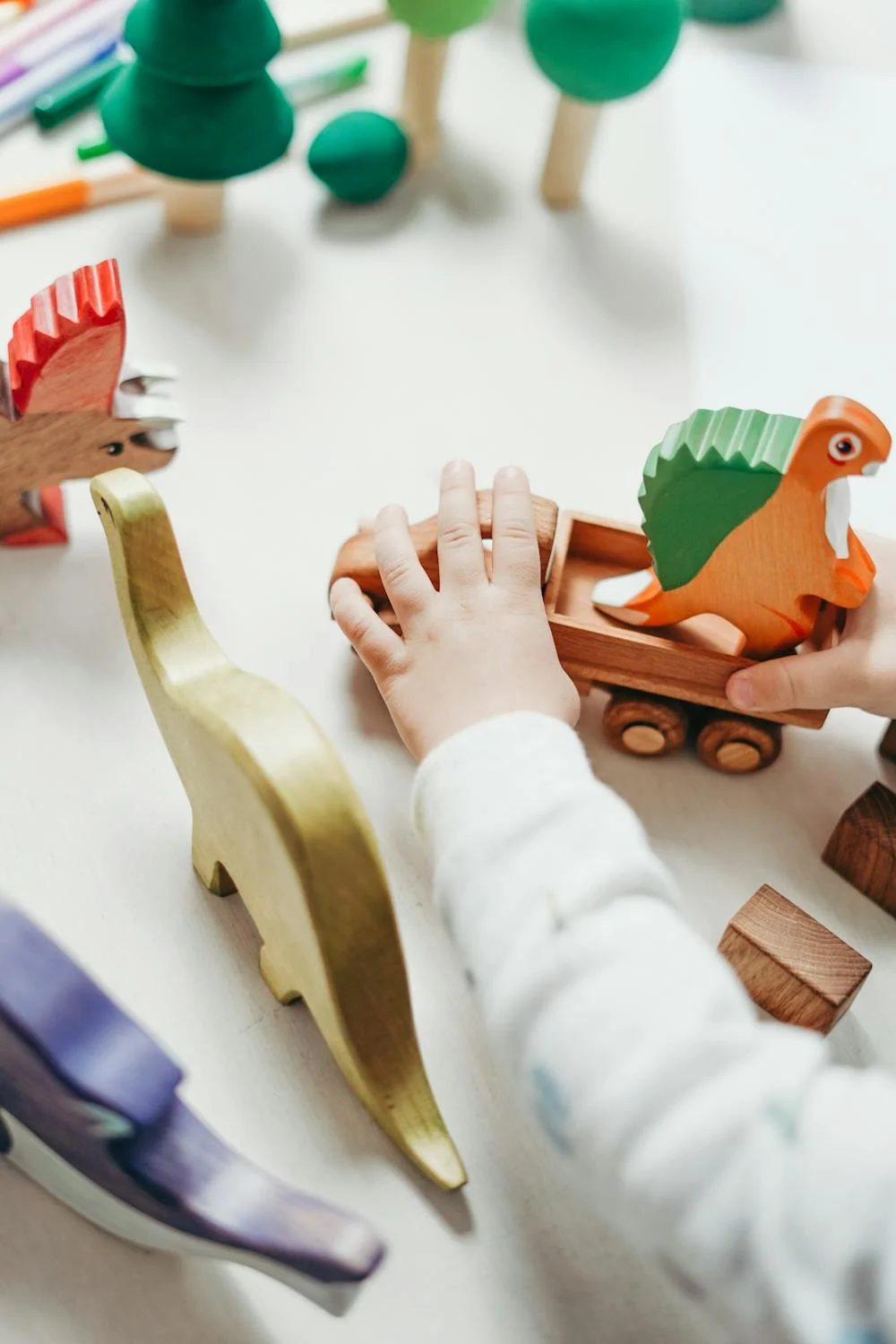 Ein Kind schiebt einen Holzwagen mit einem bunten Dinosaurier, umgeben von weiteren Holzfiguren