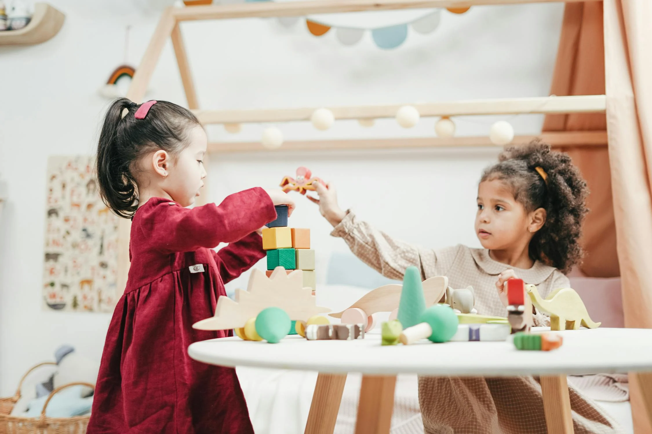 Zwei Mädchen bauen zusammen einen Turm aus bunten Holzklötzen an einem Spieltisch