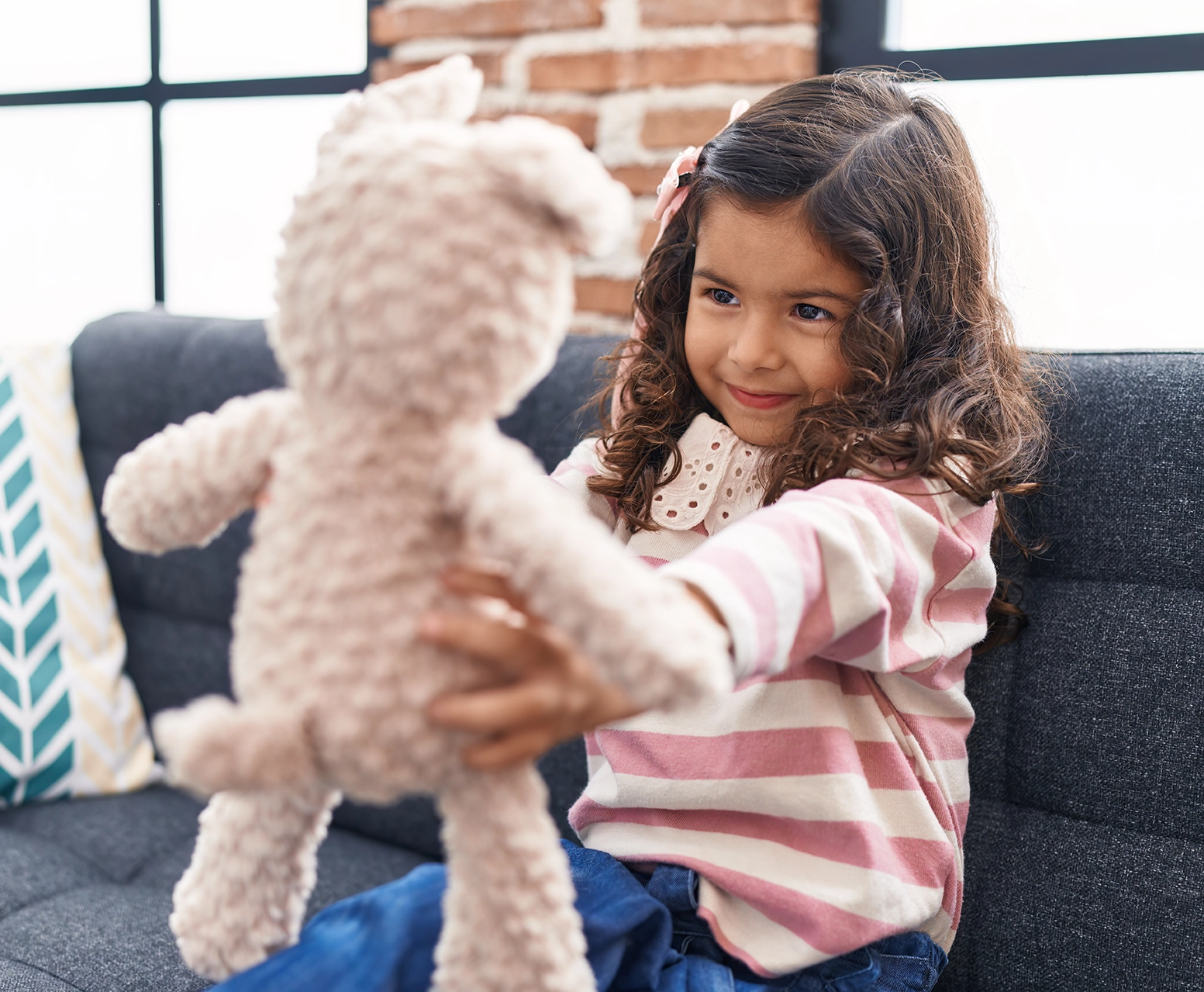Mädchen mit langen Locken hält ein Kuscheltier in beiden Händen und lächelt