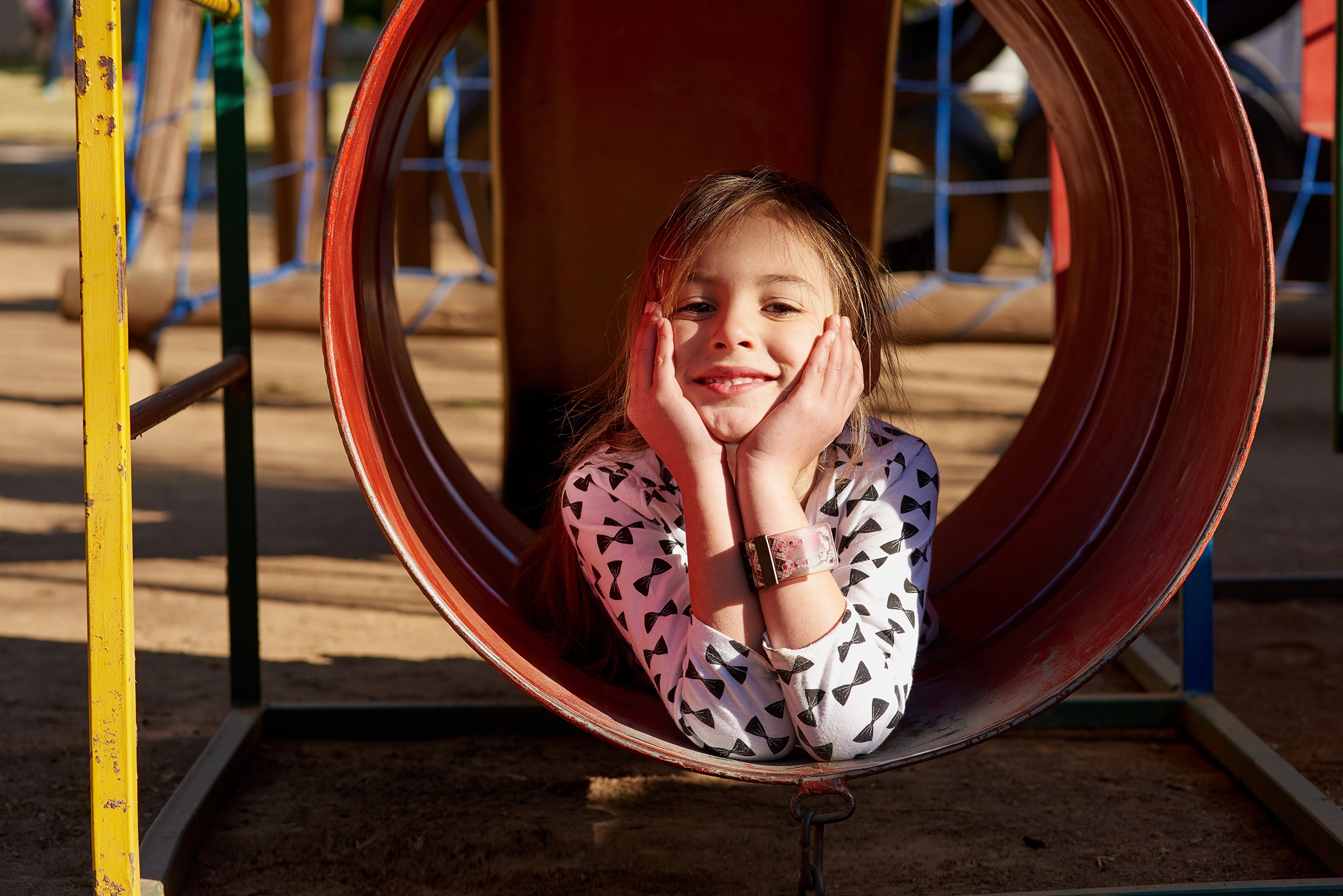 Mädchen liegt fröhlich in einem roten Tunnel auf dem Spielplatz und stützt den Kopf auf die Hände